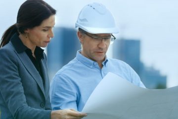 A man and woman looking at papers on top of a building.