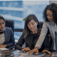 Three women are sitting at a table and one is holding papers.