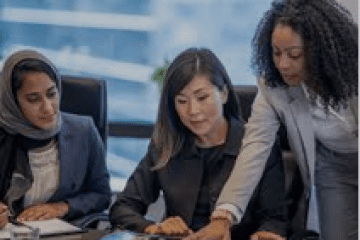 Three women are sitting at a table and one is holding papers.