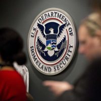 A woman and man are standing in front of the department of homeland security seal.