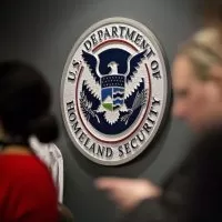 A woman and man are standing in front of the department of homeland security seal.