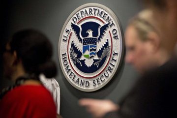 A woman and man are standing in front of the department of homeland security seal.