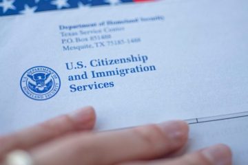 A person holding an envelope with the u. S. Citizenship and immigration services logo on it