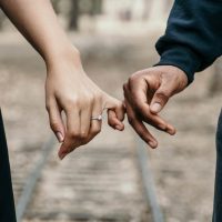 A man and woman holding hands on the train tracks.