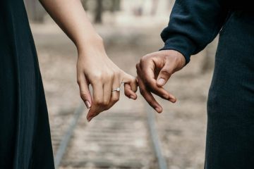 A man and woman holding hands on the train tracks.