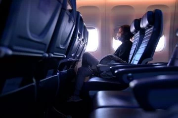 A person sitting on an airplane with their face covered.