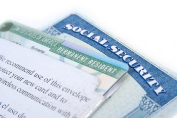 A green Permanent Resident card partially inside a Social Security envelope.