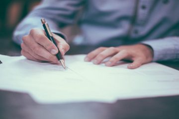 A person writing on paper with a pen.