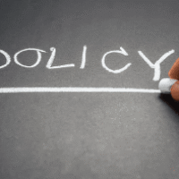 A person writing the word policy on a chalkboard.
