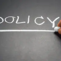 A person writing the word policy on a chalkboard.