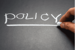 A person writing the word policy on a chalkboard. A person writing the word policy on a chalkboard.