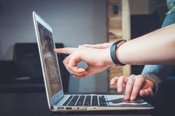 A person using their laptop with one hand and the other finger pointing at it.