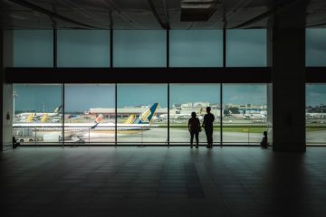 Two people standing in front of a window looking at planes.