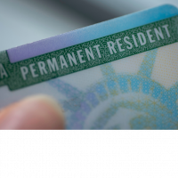 A person is holding onto the green and blue permanent resident card.