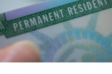 A person is holding onto the green and blue permanent resident card.