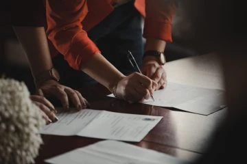 Hands signing contract on wooden table