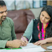 Two people collaborating on paperwork with smiles and pens.