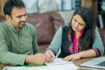 Two people collaborating on paperwork with smiles and pens.