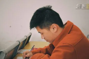 Young man writing attentively at a desk.